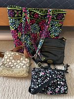 Overall lot with four purses and bags displayed - large Vera Bradley tote with floral pattern, beige Fossil bag, black Fossil purse, and smaller floral Vera Bradley bag.