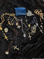 Overview of all religious medals and rosaries laid on black fabric showing various styles, bead colors, crucifixes and medallions.
