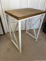 Side view of rustic side table showing wood top and white metal crossed frame base