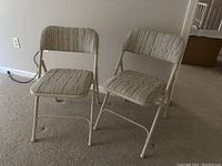 Two beige Samsonite padded folding chairs positioned side by side on carpeted floor.