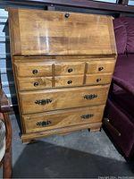 Front view of the wooden secretary desk showing the closed drop-front writing surface, three drawers, and metal hardware.