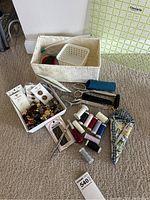 Photo showing sewing tools such as scissors, spools of thread in various colors, a cutting square ruler, and woven baskets on carpet floor.