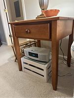 Side view of a wooden end table showing one drawer with a round knob, tapered legs, and items placed underneath.