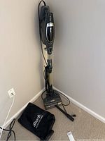 Full view of Shark Flex DuoClean vacuum in stick mode standing on carpet next to attached power cord and black Shark accessory bag containing various tools.