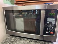 Front view of the Toshiba stainless steel microwave oven showing the door with window and digital control panel with display reading 0:00.