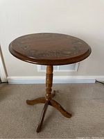 Tilting side table with round wooden top and painted fruit and foliage motif, set against carpet and wall vent