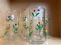 Four vintage Libbey Jubilee tulip glasses with colorful tulip flower designs arranged in a cluster inside a wooden shelf.