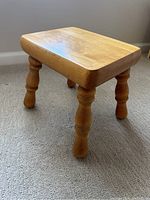 Perspective view of a small wooden stool on carpet, showing seat and legs.