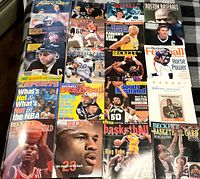 Full spread photo displaying approximately 20+ sports magazines from the 1990s laid out on a blanket. Visible covers feature basketball and football themes.