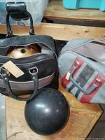 Two bowling ball bags with one bowling ball inside the black bag and one black bowling ball visible outside.
