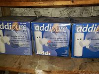 Three boxed Addipure water dispenser jugs shown side by side on a shelf with product information visible.