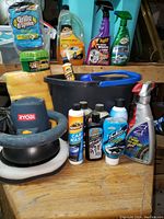 Photo of buffer, bucket, sponges, and assorted car cleaning products arranged on a wooden surface.