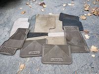 Multiple car mats laid out on ground, showing Jeep branded rubber mats and several fabric mats