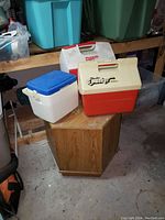 Photo of three portable coolers including Playmate, Double Tracker, and a white/blue model on a wooden surface in a garage setting.