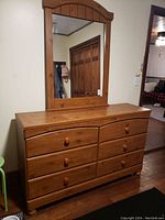 Front view of wooden dresser with attached mirror reflecting room interior.