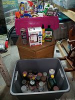 Two totes filled with assorted home improvement items including spray paint, cleaning liquids, brushes, and an LED sensor light on a wooden cabinet.