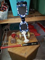 Blue and white camouflage hoverboard with two pairs of dumbbells and red and black Rawlings weighted baseball bat on a wooden table.
