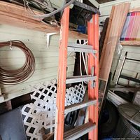 Full view of the orange fiberglass and aluminum step ladder leaning against wall showing steps and braces.