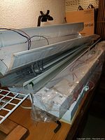 Photo showing several metal Lithonia ceiling light hoods stacked, some wrapped in plastic with wiring visible