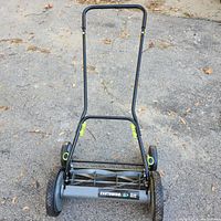 Front view of the Earthwise manual push mower showing the handle, reel blade, and wheels on an asphalt surface.