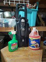 HGTV Home 1700 PSI power washer with two cleaning products, Windex Outdoor and Zep House & Siding cleaner, on a wooden surface indoors.