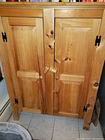 Front view of the closed solid wood pantry cabinet showing two paneled doors with black metal hinges and wood knobs and latches.