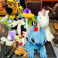 Photo showing full lot of colorful and varied cartoon character stuffed animals arranged together, including Scooby-Doo, Stitch, unicorn and Looney Tunes characters