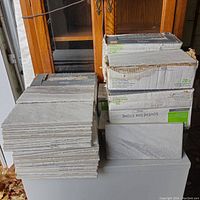 Stacks of light gray rectangular tiles with stone pattern, some loose, some in original boxes.