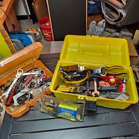 Wide view showing two plastic toolboxes with assorted hand tools and hardware items on a table.