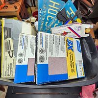 Photo showing boxed sanding sheets, an air inflator compressor box, and other items in a black tote