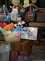 Wide view of assorted vintage nursery items showing wooden rocking horse, plush Mickey Mouse, Raggedy Ann doll, colorful butterfly wings plush, musical mobile box, photo frame, and Barnes & Noble albums