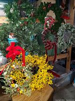 Photo showing multiple decorative wreaths including green pine needle wreaths with red berry accents and velvet bows, yellow flower wreath, and eucalyptus leaf wreath.
