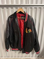 Full view of black leather bomber jacket with red interior, hanging on hanger.