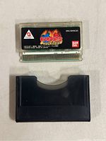 Front view of clear plastic game cartridge with Japanese Kinnikuman Muscle Tag Match 2 label, and black plastic protective case below.