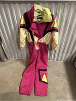 Full view of the vintage ladies snow suit hanging on a rack indoors, showing front zipper and color block pattern