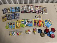 Overall flat lay of mixed sealed and loose Pokemon cards with pins and tokens on a beige table.