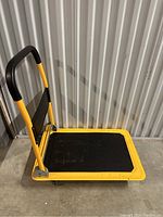 Side angled view of the yellow folding platform rolling dolly showing handle and platform surface