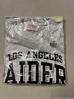 Gray Los Angeles Raiders shirt front view, folded and sealed in original packaging with brand label visible.