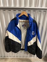 Front view of vintage Toronto Blue Jays windbreaker jacket showing blue, black, and white color blocking with embroidered Blue Jays patch on front left chest.