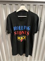 Front view of black Rolling Stones T-shirt with colorful printed logo and text in blue, red, yellow.