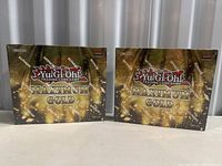 Front view of two sealed Yu-Gi-Oh Maximum Gold booster boxes side by side showing gold and black packaging with Konami branding.