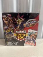 Front view of sealed Yu-Gi-Oh Monster Box showing 9 booster packs 1 legacy pack text and character artwork