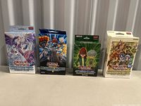 Four sealed Yu-Gi-Oh! packages including booster packs and structure decks shown side by side, unopened with protective blister packs or boxes.