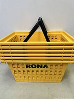 Stack of six new yellow Rona plastic shopping baskets with black handles, RONA logo visible on front basket.