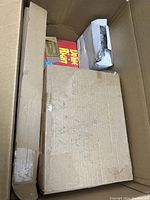 Photo showing top view of packed cardboard box with several smaller boxes and packages including a white electronic device and wrapped items.