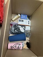 Box containing various items including PlayStation controller, tumblers, speaker, and small household accessories