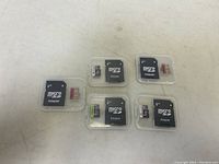 Five micro SD cards each with a black micro SD adapter in a clear case, arranged on a white surface.