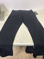 Front full view of black men's jeans laid flat on a surface to show overall condition and style.