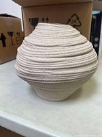 Full view of the vase showing its coil textured, rounded, natural beige design