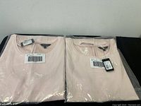 Photo of two RW & CO pink sleeveless shirts, medium and small, in plastic packaging.